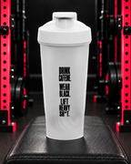White protein shaker with spaced black Drink Caffeine Wear Black Lift Heavy Shit slogan in the WWLW gym