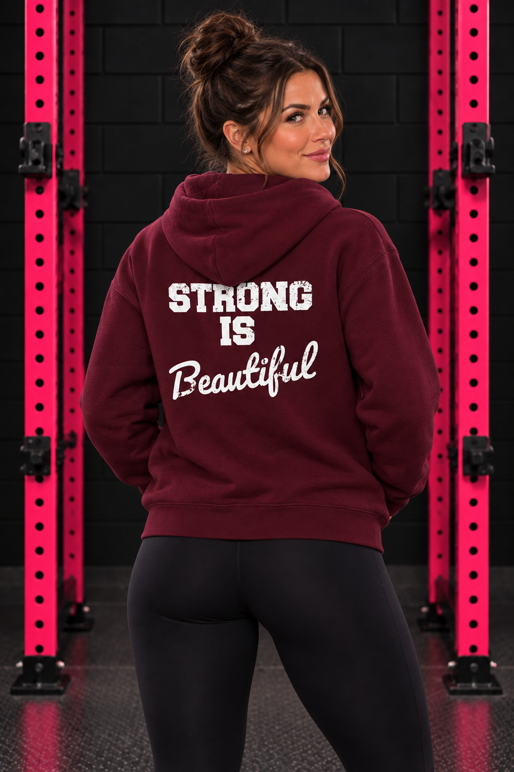 Maroon Strong Is Beautiful hoodie back print, female model between pink squat rack uprights