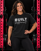 Built Different Tee — Women's 6-Ounce Heavyweight Tee, vintage black, front view on muscular woman in black gym with pink racks