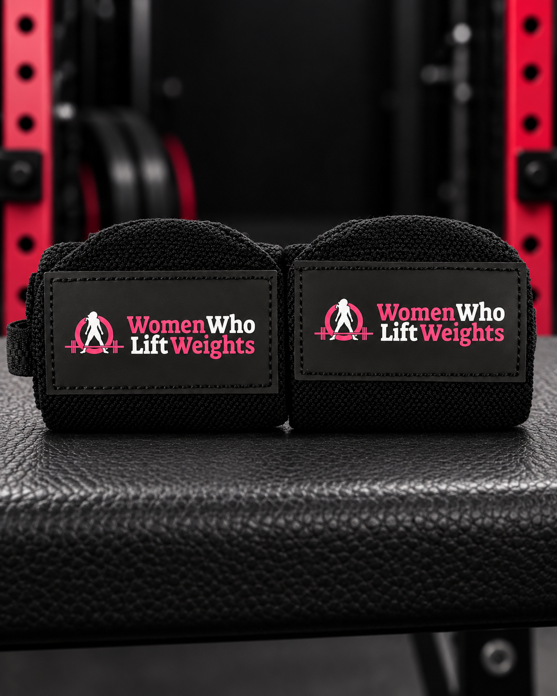 Pair of black Women Who Lift Weights wrist wraps with pink and white logo patches.