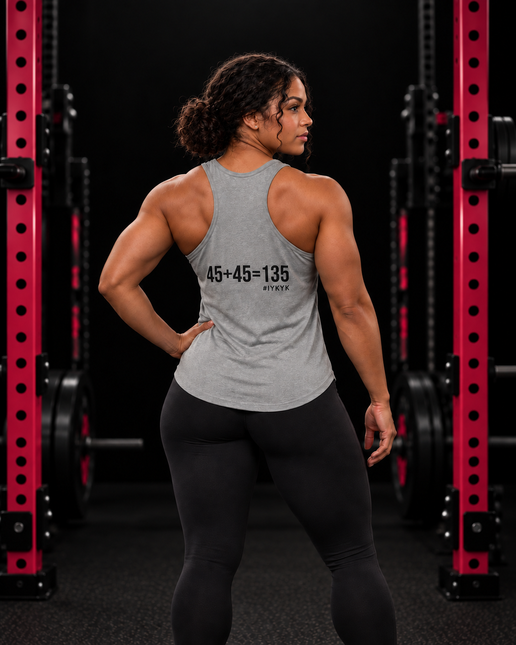 45 + 45 = 135 racerback tank, gray with black back print, worn by an athletic woman in a black and pink gym.
