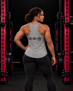 45 + 45 = 135 racerback tank, gray with black back print, worn by an athletic woman in a black and pink gym.