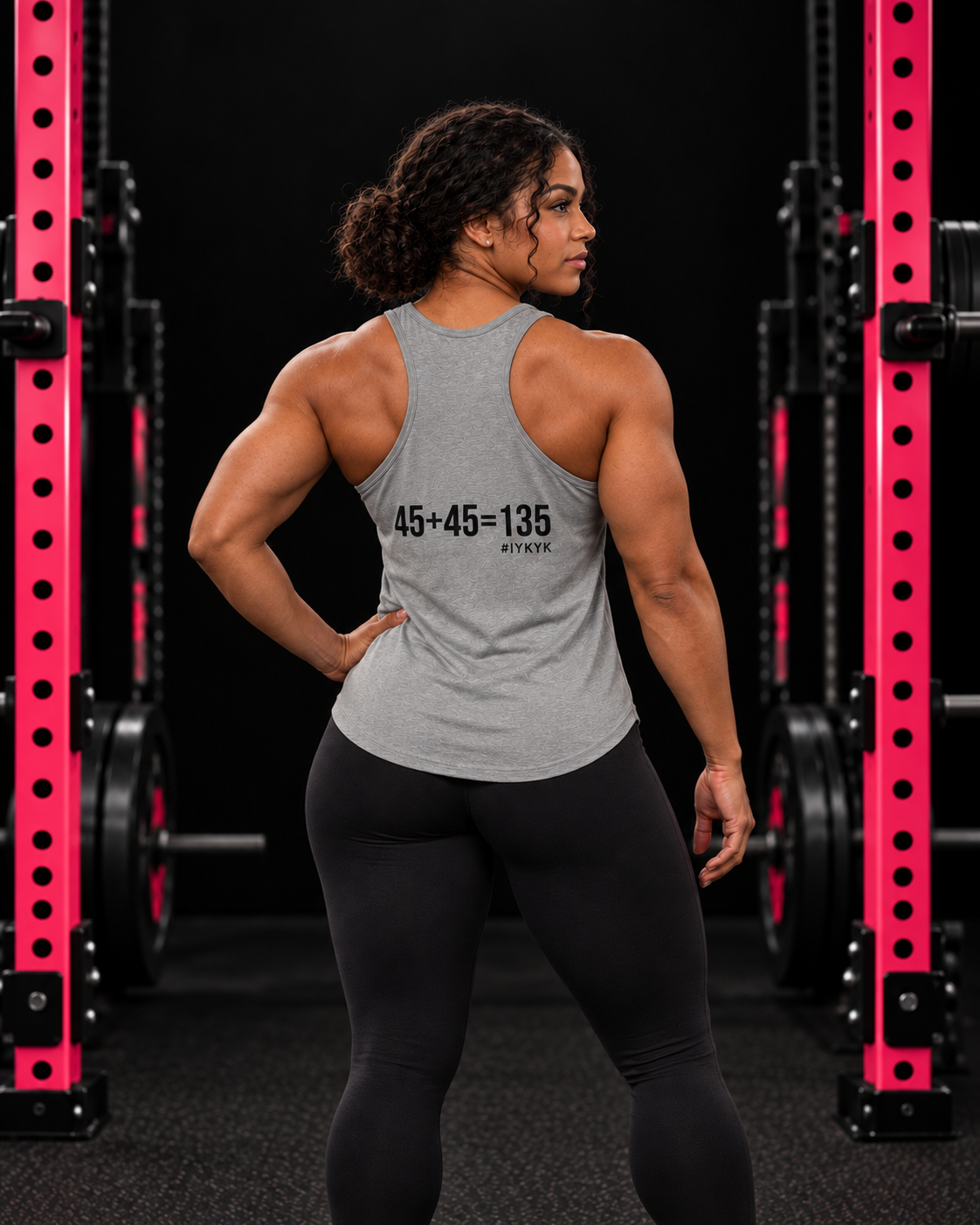 45 + 45 = 135 racerback tank, gray with black back print, worn by an athletic woman in a black and pink gym.