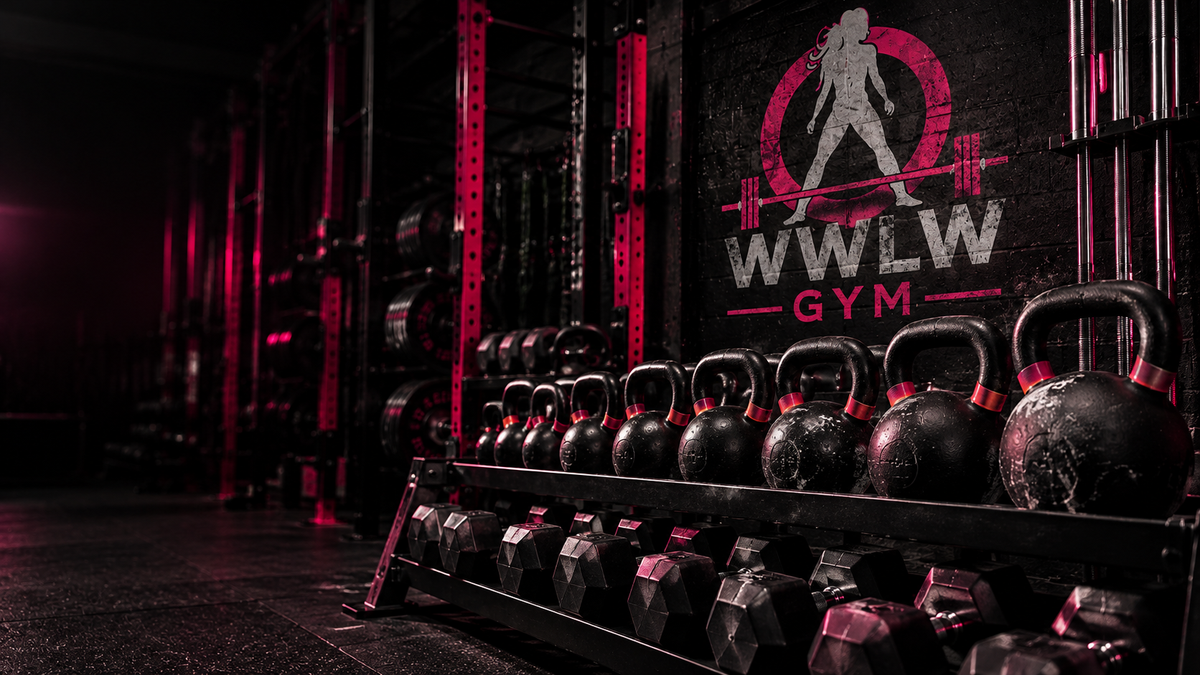 Kettlebells and Dumbbells on a rack in the WWLW gym with the Women Who Lift Weights logo